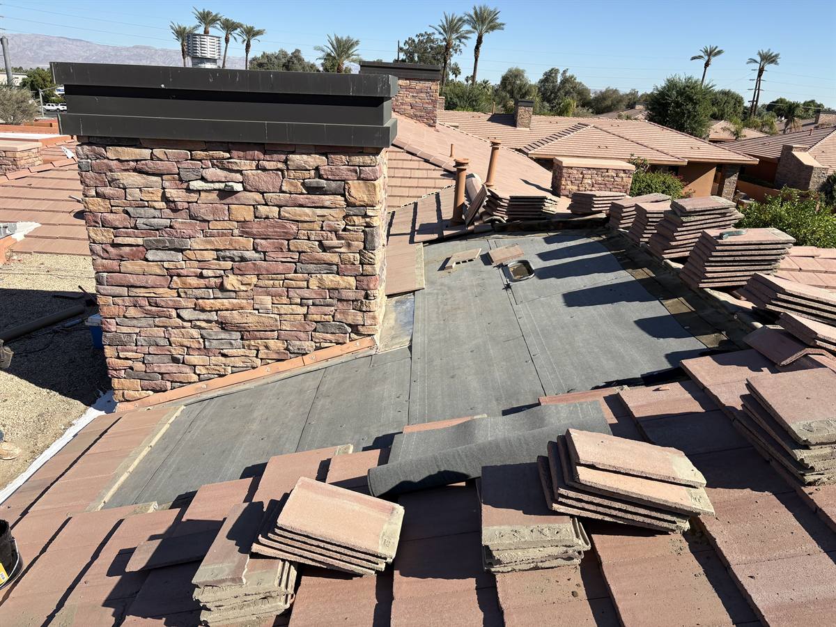Tile re-roof underway around a stacked stone chimney