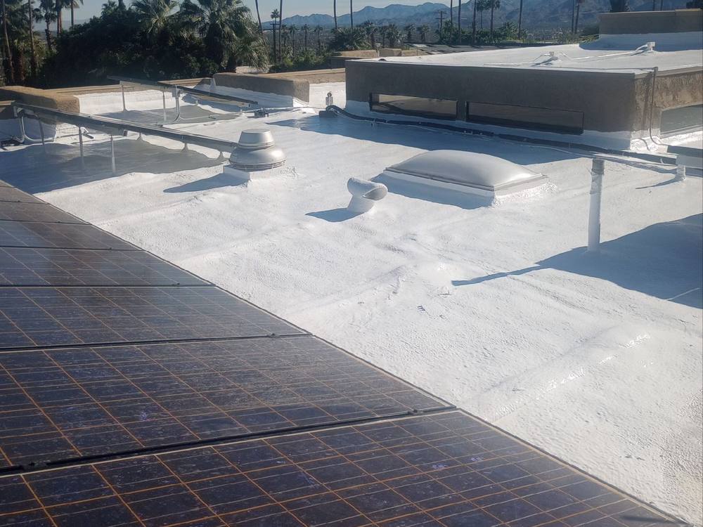 White reflective cool roof coating around solar panels with palms and mountains beyond